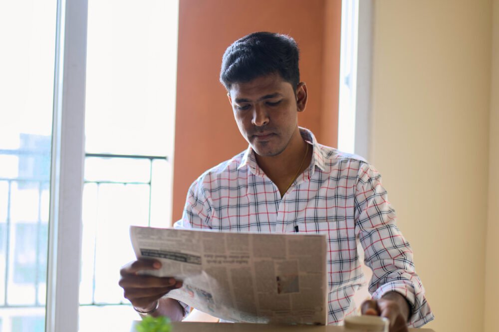 Indoor cafe, man reading newspaper at table, sunlight through window, soft morning light, editorial travel photo, one person.